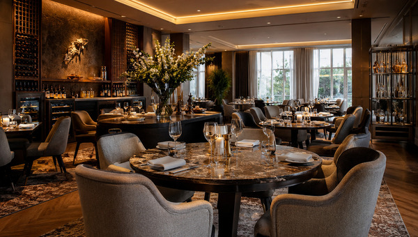 Elegancka sala restauracyjna hotelu z marmurowymi stolikami, tapicerowanymi krzesłami i nastrojowym oświetleniem, budująca prestiżową markę poprzez wystrój.