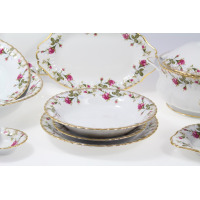 Serwis obiadowy Chodzież Iwona B013 dla 12 osób. Biała porcelana z delikatnym motywem róż i złotym wykończeniem brzegów. Widoczne talerze, półmisek i waza.