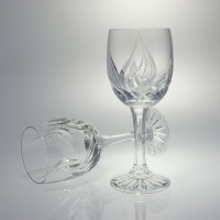Dwa kieliszki kryształowe do wina Monica marki Zawiercie. Jeden stoi pionowo, drugi leży obok, ukazując eleganckie szlifowane wzory na przezroczystym szkle.