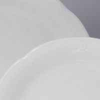 Zbliżenie na białe talerze z serwisu obiadowego Kamelia Chodzież. Widoczne subtelne, wytłaczane zdobienia na krawędziach klasycznej porcelany dla 12 osób.