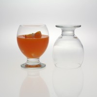 Szklanki na nodze NECTAR marki LAV o pojemności 280 ml. Jedna szklanka wypełniona pomarańczowym napojem z cząstką owocu, obok druga odwrócona dnem do góry.