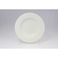 Talerz do pasty 30 cm BANQUET marki RAK Porcelain w kolorze kremowej bieli. Okrągłe naczynie z szerokim rantem ustawione na przezroczystym stojaku, widok od