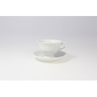Biała filiżanka do herbaty 0,22 l z serii Iwona marki Chodzież. Klasyczna porcelana o falistym brzegu, ustawiona na pasującym spodku, widok z profilu.