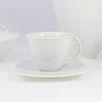 Biały porcelanowy zestaw kawowy Akcent marki Chodzież. Na pierwszym planie filiżanka na kwadratowym spodku, obok cukiernica z pokrywką i fragment dzbanka.