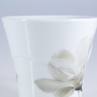 Zbliżenie na górną część białego porcelanowego kubka Lubiana 300 ml z serii 6474 Magnolia. Delikatny, szary motyw kwiatowy zdobi gładką powierzchnię naczynia.