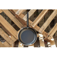 Patelnia 32 cm CHOC Resto Induction marki DeBuyer z czarną powłoką nieprzywierającą, umieszczona pionowo na drewnianych paletach. Widoczne logo DeBuyer na