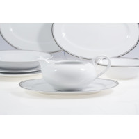 Sosjerka z serwisu obiadowego Yvonne marki Chodzież na spodku, w otoczeniu białych talerzy z delikatnym srebrnym obrzeżem. Elegancka porcelana dla 12 osób.