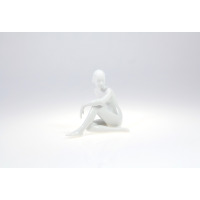 Biała figurka porcelanowa ZAMYŚLONA 0001 marki Ćmielów. Minimalistyczna rzeźba przedstawia siedzącą postać kobiecą o gładkiej, błyszczącej powierzchni.