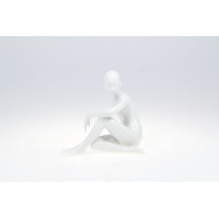 Biała figurka porcelanowa ZAMYŚLONA 0001 marki Ćmielów. Minimalistyczna rzeźba przedstawia siedzącą postać kobiecą o gładkiej, błyszczącej powierzchni. Widok z