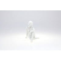 Biała figurka porcelanowa ZAMYŚLONA 0001 marki Ćmielów. Subtelna rzeźba przedstawia siedzącą, nagą kobietę w zamyślonej pozie, wykonaną z gładkiej, błyszczącej