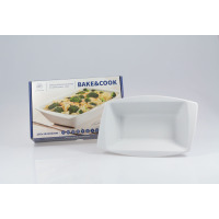 Białe porcelanowe naczynie do zapiekania Lubiana Rumba 260x162x61mm obok opakowania z napisem Bake&Cook. Widoczny zestaw z produktem gotowym do użycia w kuchni.