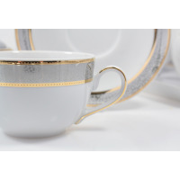 Zbliżenie filiżanki z zestawu kawowego dla 12 osób G627 Yvonne marki Chodzież. Biała porcelana ze złotym zdobieniem i szarym ornamentem, w tle pasujący spodek.