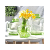 Zielony szklany wazon Latitude 28 cm od Krosno Glass S.A. z bukietem żółtych żonkili, ustawiony na białym stole obok dwóch innych przezroczystych naczyń.