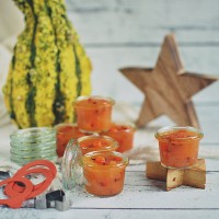 Słoiki 50 ml WECK Mini-Sturz wypełnione pomarańczową konfiturą z owocami, ustawione na drewnianej gwieździe obok ozdobnej dyni, gumowych uszczelek i metalowych