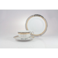 Zestaw do herbaty Ćmielów E551 Bolero Princess: biała porcelanowa filiżanka na spodku oraz duży talerz z eleganckim złotym i szarym zdobieniem na obrzeżach.