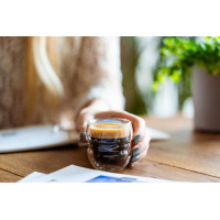 Zbliżenie na szklankę do espresso z podwójną ścianką Sferico od Vialli Design wypełnioną aromatyczną kawą, trzymaną w dłoni przez osobę przy drewnianym stole.