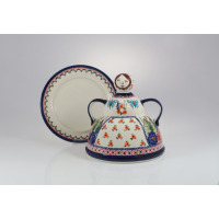 Ceramiczna baba do sera Bolesławiec GU-847 o średnicy 19,2 cm z motywem kwiatów i motyli, z uchwytem w kształcie głowy lalki, ustawiona przed pasującym