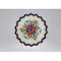 Ceramiczny talerz z falbanką Bolesławiec GU-1332A o średnicy 32,4 cm. Kremowe tło zdobi ręcznie malowany wzór w czerwone i niebieskie kwiaty, zielone liście i