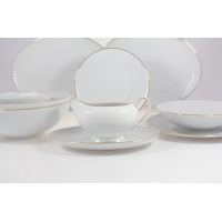 Serwis obiadowy Chodzież Dalia Złota linia dla 12 osób. Biała porcelana z delikatnym prążkowanym wzorem i złotym wykończeniem brzegów, wyeksponowana na stole.