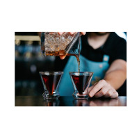 Barman nalewa ciemny koktajl z mieszadła do dwóch kieliszków do martini z podwójną ścianką SOHO marki Vialli Design, eksponując ich nowoczesny, szklany design.