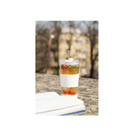 Szklany kubek termiczny Vialli Design FUORI 600 ml z białą opaską i słomką, wypełniony napojem z owocami, stoi na kamiennym murku obok otwartej książki.