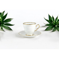 Biała porcelanowa filiżanka do kawy 0,17 l ze spodkiem Ćmielów Alaska, ozdobiona eleganckim złotym obrzeżem i uchwytem, ustawiona symetrycznie między dwoma