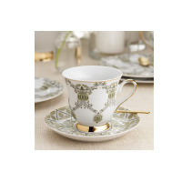 Elegancka filiżanka ze spodkiem z zestawu do kawy Ćmielów ASTRA Meander. Biała porcelana z subtelnym zielono-szarym wzorem roślinnym i złotymi wykończeniami.