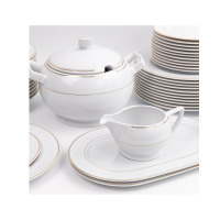 Elegancki zestaw obiadowy Gracja WA-151 marki Waza. Biała porcelana ze złotym zdobieniem, waza z pokrywką, sosjerka na owalnym półmisku oraz stosy talerzy.