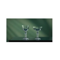 Dwa kieliszki Onis Tiki Clear o pojemności 200 ml z ozdobną nóżką, ustawione na ciemnym blacie na tle w odcieniach zieleni. Widok z przodu.