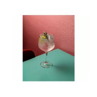 Kieliszek Gin & Tonic Skyline marki Onis o pojemności 590 ml wypełniony drinkiem z lodem, cytryną i gałązką rozmarynu, ustawiony na turkusowym blacie.