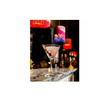 Kieliszek martini Perfection marki Onis o pojemności 240 ml z koktajlem i oliwkami, ustawiony na marmurowym blacie w klimatycznym barze z kolorowymi lampami.