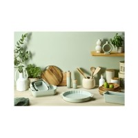 Jasnozielony młynek do soli Peugeot Boreal 12 cm w otoczeniu ceramicznych naczyń kuchennych, drewnianych desek i świeżych ziół na jasnym blacie.