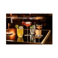 Cztery eleganckie koktajle w szklankach i kieliszkach Schott Zwiesel Rooftop 245 ml na czarnym, lustrzanym blacie w nastrojowym oświetleniu restauracyjnym.