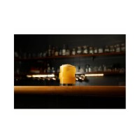 Szklanka The Glitch marki Onis o pojemności 355 ml z wypełnionym żółtym koktajlem, ustawiona na drewnianym barze w tle z półkami pełnymi alkoholi.