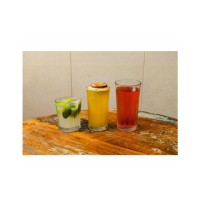 Trzy szklanki Cooler 470 ml marki Onis z serii Mosaic na drewnianym stole. Wypełnione kolorowymi koktajlami: mojito, napojem z marakują i czerwonym drinkiem.