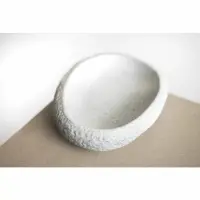Kamienny talerz Verlo Stone o wymiarach 24x19x5 cm w jasnoszarym kolorze. Naturalna, porowata tekstura kamienia z gładkim, wgłębionym wnętrzem na beżowym tle.