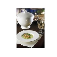 Talerz głęboki White Gold marki RAK Porcelain o pojemności 620 ml z zupą i grzankami, ustawiony na ozdobnym spodku obok wazy i kieliszka na ciemnym stole.
