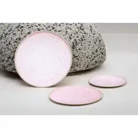 Trzy talerze płytkie Sweet marki Verlo o średnicy 21 cm z różowym, nakrapianym wzorem, ustawione na jasnym tle obok szarego, kamiennego elementu dekoracyjnego.