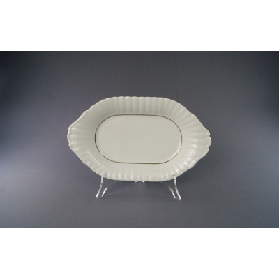 Owalny półmisek Chodzież Iwona 24 cm z białej porcelany o karbowanym brzegu, zdobiony subtelną złotą linią, wyeksponowany na przezroczystym stojaku na szarym