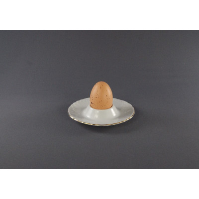 Kieliszek na jajko z podstawką Ćmielów 3604 ROCOCO. Biała porcelana ze złotym rantem i tłoczonym wzorem, w której umieszczono brązowe jajko w kropki. Widok