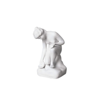 Biała figurka porcelanowa U ŹRÓDŁA 0001 marki Ćmielów. Przedstawia klęczącą kobietę czerpiącą wodę, wykonaną z matowej porcelany o eleganckim, klasycznym stylu.