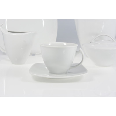 Biały zestaw kawowy Chodzież Akcent dla 12 osób. Zbliżenie na filiżankę na kwadratowym spodku, w tle dzbanek i cukiernica z tej samej porcelanowej kolekcji.