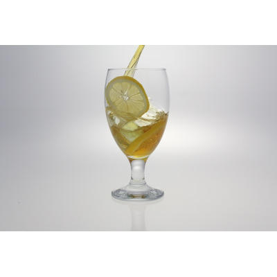 Szklanka na nodze EMPIRE marki LAV wypełniona mrożoną herbatą z lodem i plastrem cytryny. Eleganckie naczynie o pojemności 590 ml w trakcie napełniania napojem.