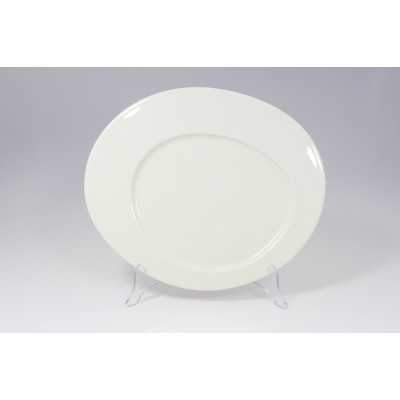 Owalny talerz płytki CAYENNE 34 cm marki RAK Porcelain w kolorze kremowej bieli. Naczynie o minimalistycznym designie ustawione na przezroczystym stojaku.