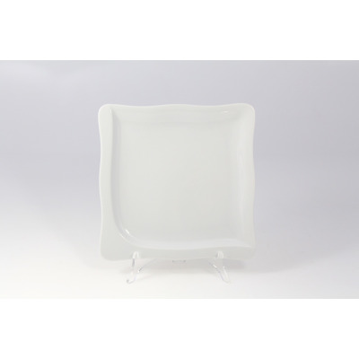 Biały talerz płytki GOURMET marki Lubiana o średnicy 22 cm. Kwadratowe naczynie z porcelany o delikatnie falowanych brzegach, wyeksponowane na przezroczystym