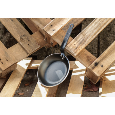 Patelnia 20 cm CHOC Resto Induction marki DeBuyer z czarną powłoką nieprzywierającą, oparta na drewnianych paletach. Na rączce widoczne tłoczone logo de BUYER.
