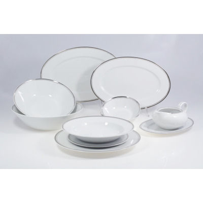 Serwis obiadowy Chodzież G238 YVONNE dla 12 osób. Biała porcelana z delikatnym srebrnym obrzeżem, obejmująca półmiski, misy, talerze i sosjerkę na podstawce.