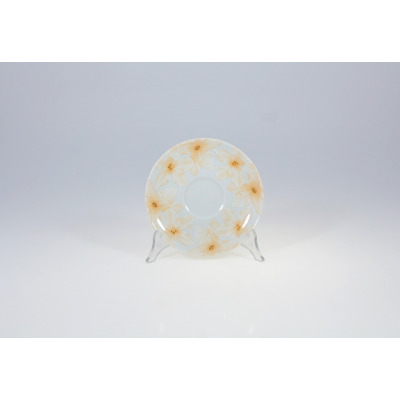 Porcelanowy spodek Chodzież 9542 YVETTE o średnicy 15,7 cm. Naczynie zdobi delikatny motyw kwiatowy w odcieniach beżu i żółci na jasnym tle, ustawione na