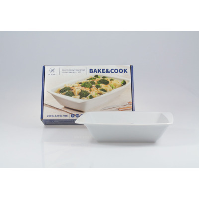Białe porcelanowe naczynie do zapiekania Lubiana Rumba 260x162x61mm ustawione przed opakowaniem z nadrukiem potrawy Bake&Cook. Widok z przodu na produkt.