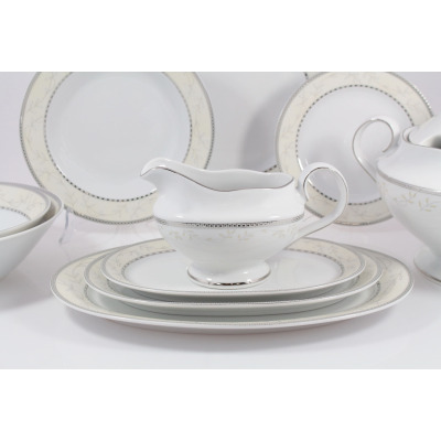 Elegancka sosjerka z serwisu obiadowego B601 Astra marki Ćmielów, ustawiona na owalnym półmisku. Biała porcelana z delikatnym roślinnym wzorem i srebrnym
